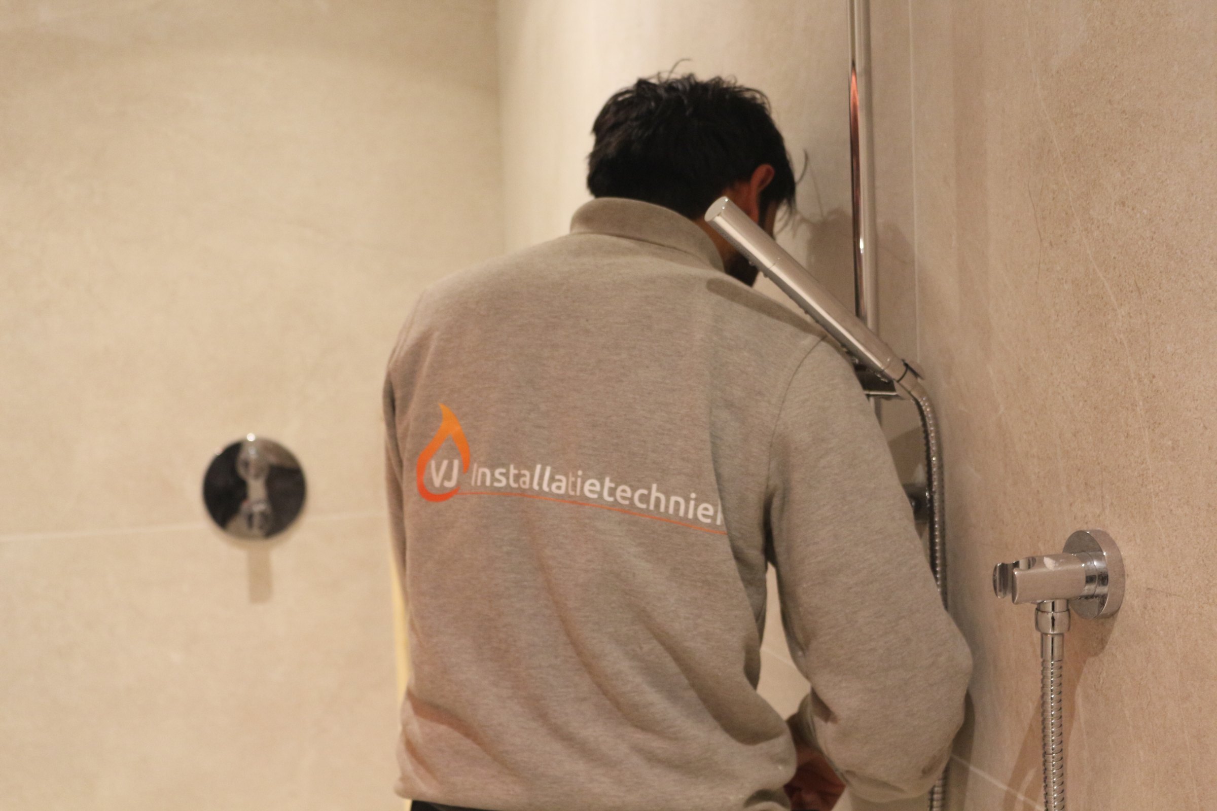 Monteur van VJ Installatietechniek monteert een douchegarnituur in een afgewerkte badkamer