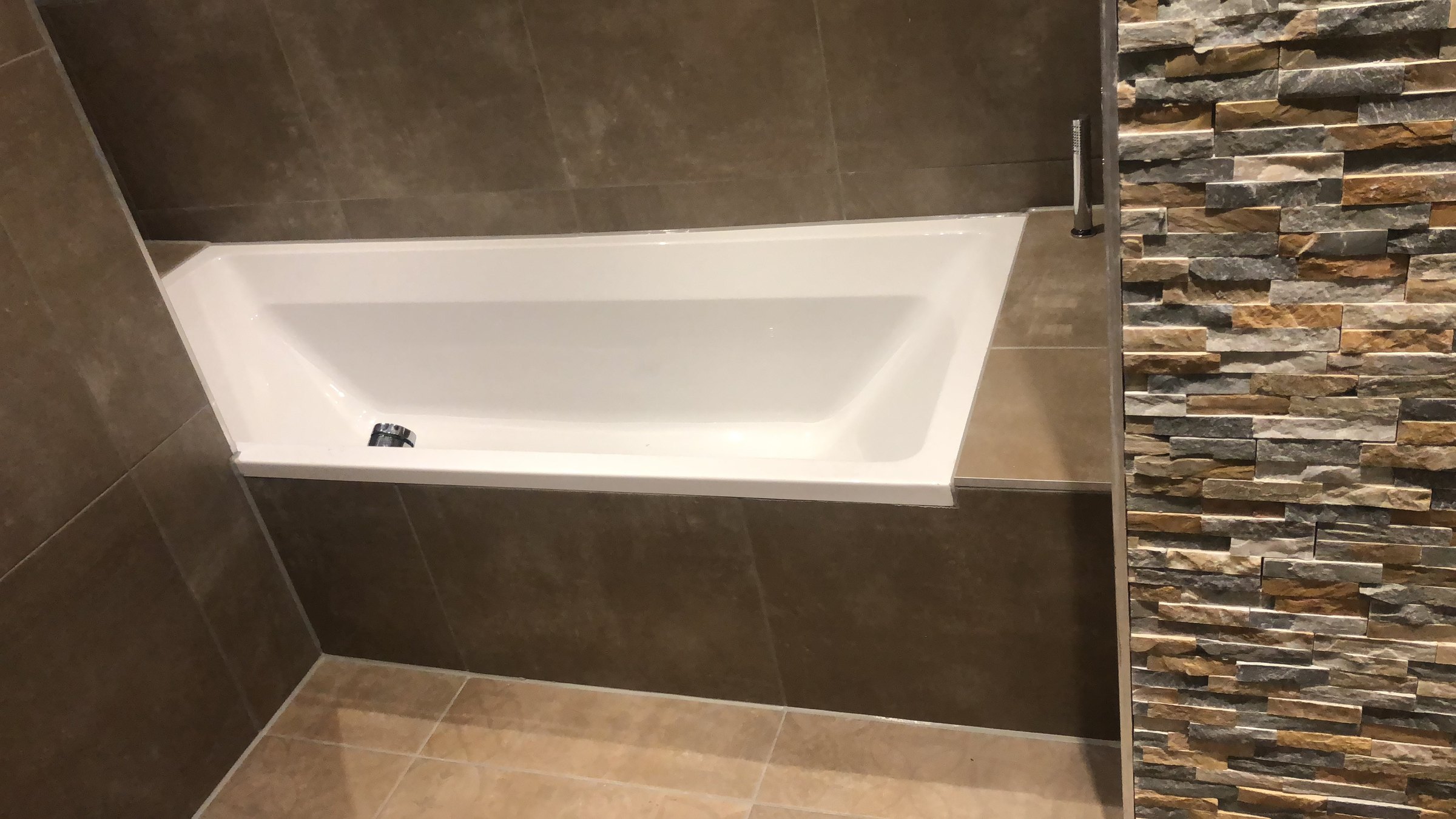 Badkamer in Zeewolde met ingebouwd bad tegen een natuurstenen wand